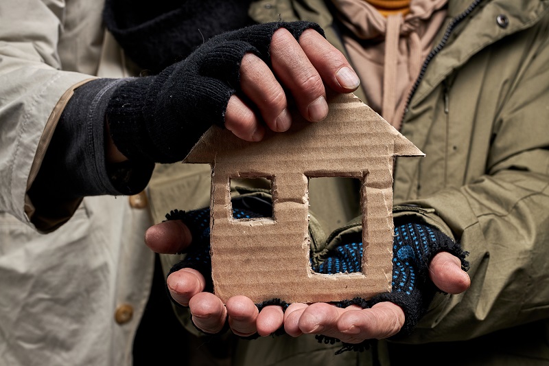 unhoused people holding a home made from cardboard